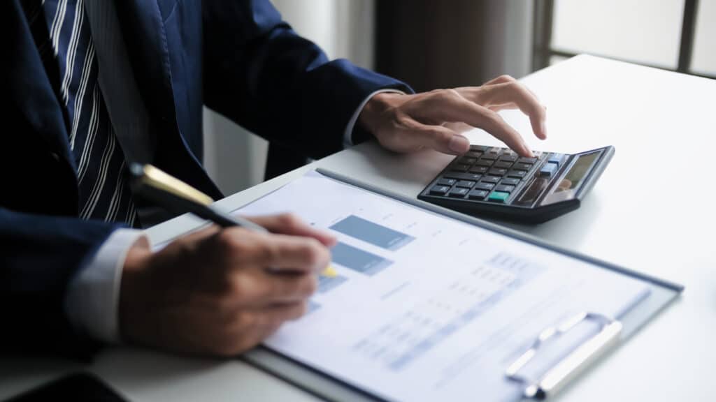 Businessperson in a suit uses a calculator while reviewing financial documents at a desk.