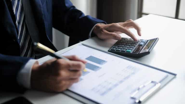 Businessperson in a suit uses a calculator while reviewing financial documents at a desk.