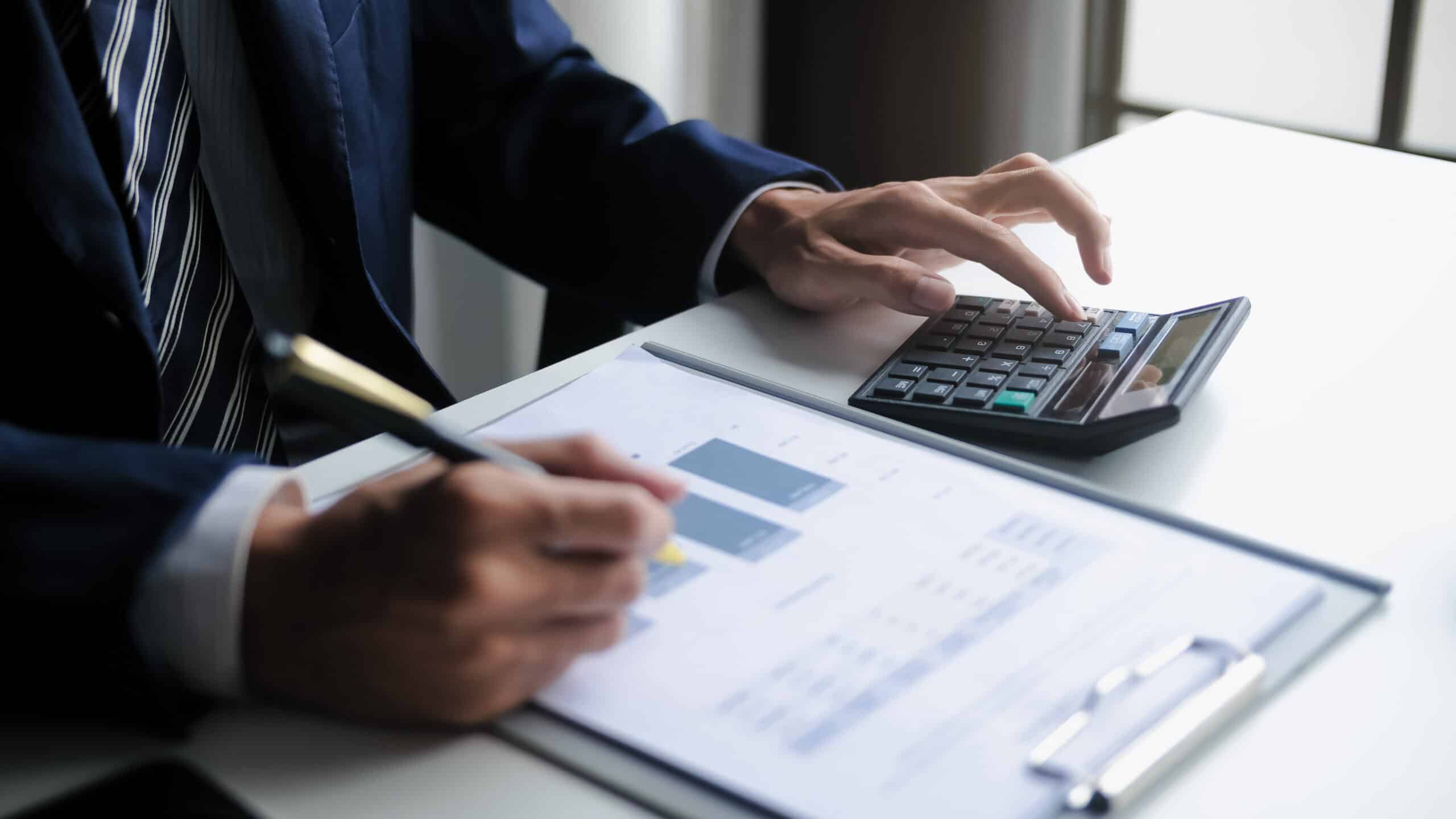 Businessperson in a suit uses a calculator while reviewing financial documents at a desk.